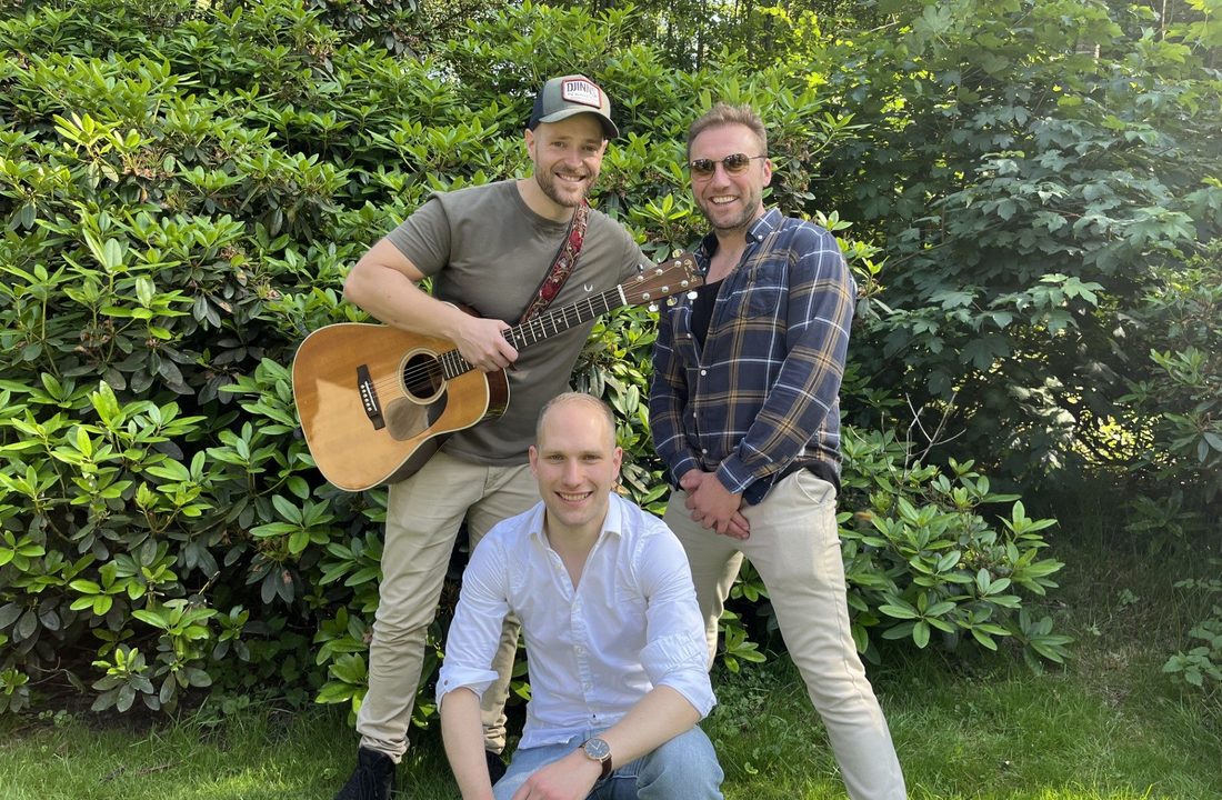 Three musicians posing outdoors with an acoustic guitar